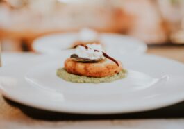 A close-up view of a gourmet dish featuring a golden patty topped with cream and a chili, served on a green sauce