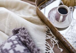 A cozy arrangement of a blanket, decorative pillow, and a cup of coffee on a tray.