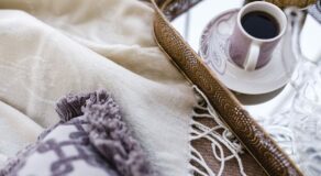 A cozy arrangement of a blanket, decorative pillow, and a cup of coffee on a tray.