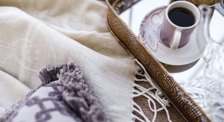 A cozy arrangement of a blanket, decorative pillow, and a cup of coffee on a tray.